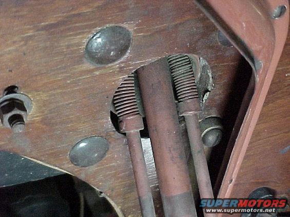 Close-up of metal rods and springs on a wooden surface, with a Supermotors logo in the corner