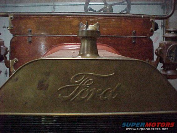 1912 Ford Model T radiator with Ford script and hood ornament. Wooden dashboard and steering wheel visible