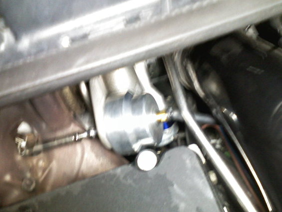 Close-up of a silver engine component with blue accents and hoses attached