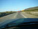 1988 Ford Bronco - A red pickup truck tows a trailer down a highway under a clear blue sky.