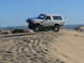 1988 Ford Bronco - White 1988 Ford Bronco airborne over a sand dune, kicking up dust.