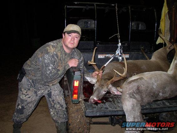 guy in camo leaning on tailgate of utility vehicle with two deer in the back
