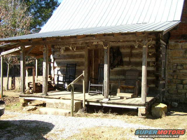 Log cabin porch with two rocking chairs and a wooden bench. Antlers are mounted on the porch posts
