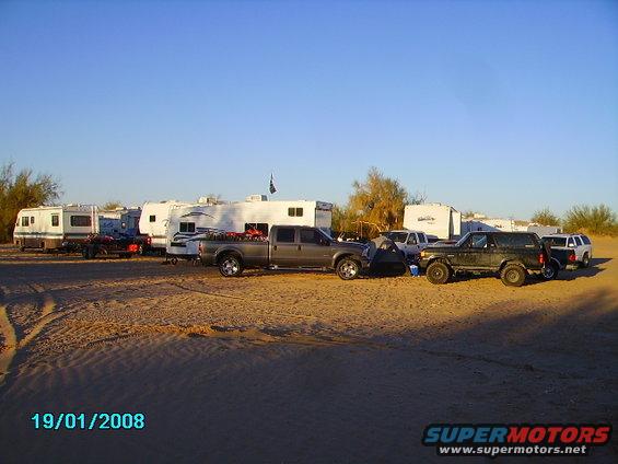 Several RVs and trucks parked on sand, with a dark SUV in the foreground