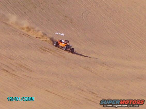 Orange dune buggy driving on a sand dune, kicking up dust