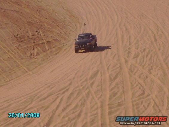 Dark pickup truck driving on sand dunes, front view