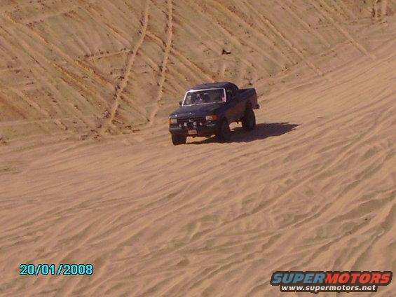 Dark blue 1990 Ford Bronco driving on sand dunes