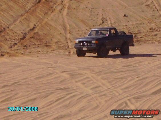 1990 Ford Bronco driving on sand dunes, 3/4 front view