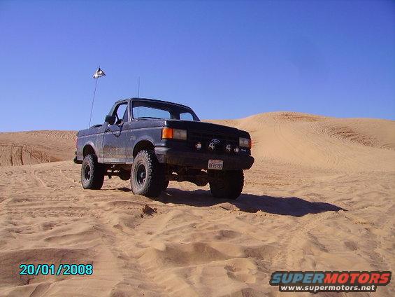 Black pickup truck with pirate flag on sand dunes, 1990 model year