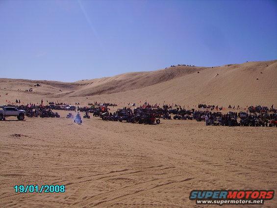 Many off-road vehicles and dune buggies parked on sand dunes under a clear blue sky. Date stamp 19/01/2008