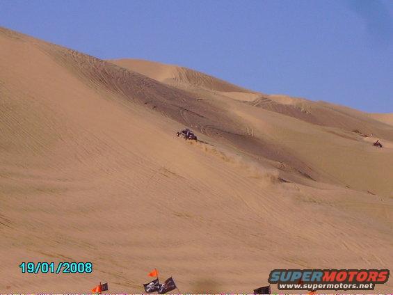 dune buggy kicking up dust on a sand dune, another vehicle in distance