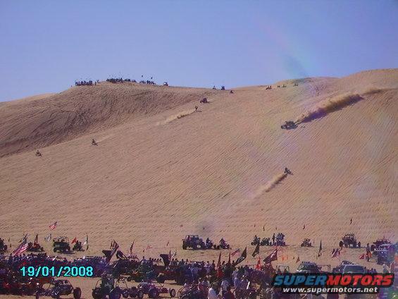 Off-road vehicles racing up sand dunes under a clear blue sky