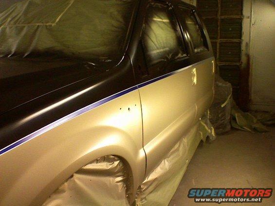 Side view of an SUV with its windows taped off and body covered in masking paper, ready for paint