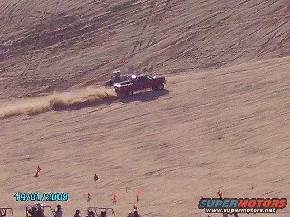 red pickup truck kicking up sand while driving on a dune, with a date stamp of 19/01/2008 and a Supermotors logo