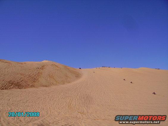 Sand dunes with ATVs and people riding on them under a clear blue sky. Date stamp 20/01/2008