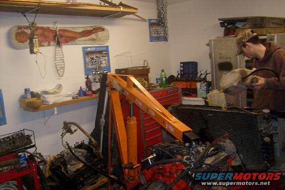 Garage scene with engine parts, engine hoist, and a person working on a radiator