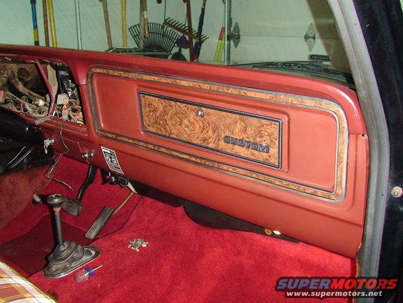 1979 Ford F-150 interior showing dashboard with woodgrain trim and 'CUSTOM' badge, red carpet, and manual shifter
