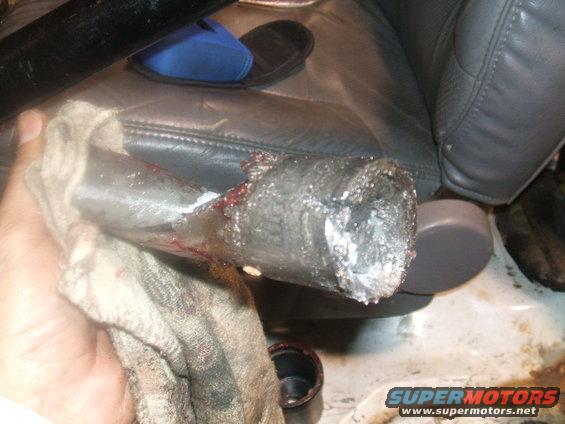 Damaged metal pipe held with a rag, showing blood and metal shavings. Interior of a vehicle is visible in the background