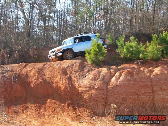 Light blue Toyota FJ Cruiser driving off-road on a dirt hill