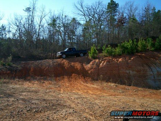 Dark pickup truck driving on a dirt mound with trees in the background