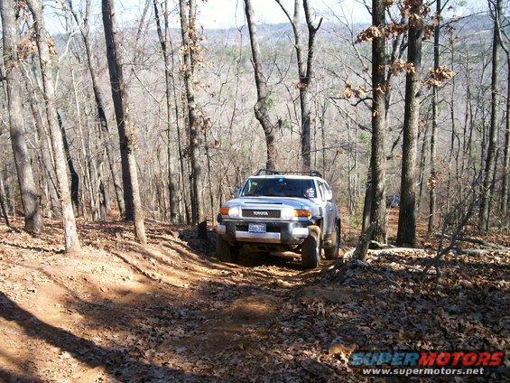 Silver Toyota FJ Cruiser driving on a dirt trail through a forest
