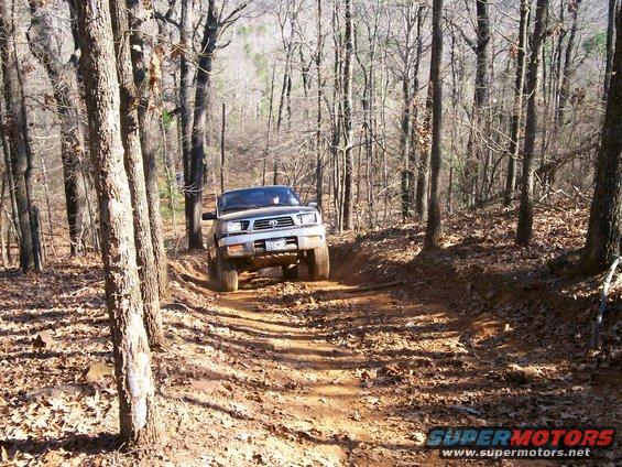 Silver Toyota Tacoma driving on a dirt path in a forest, front 3/4 view