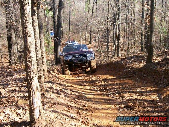 Dark SUV with off-road modifications on a wooded trail. Text on grille reads "TOYOTA"