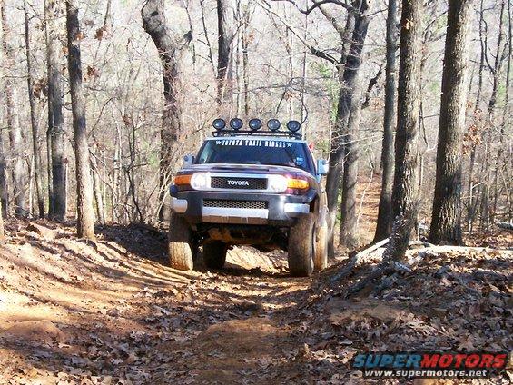 Toyota FJ Cruiser with roof lights driving on a wooded trail. Reads 'TOYOTA TRAIL RIDERS'