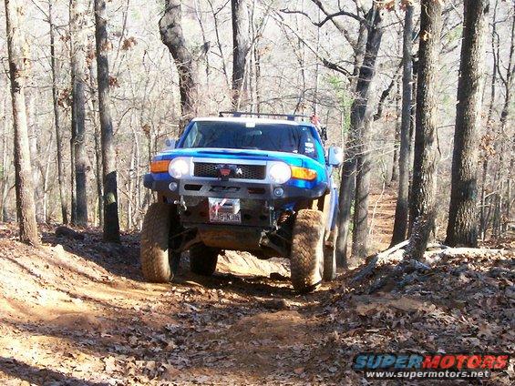 Blue Toyota FJ Cruiser driving on a dirt path through trees