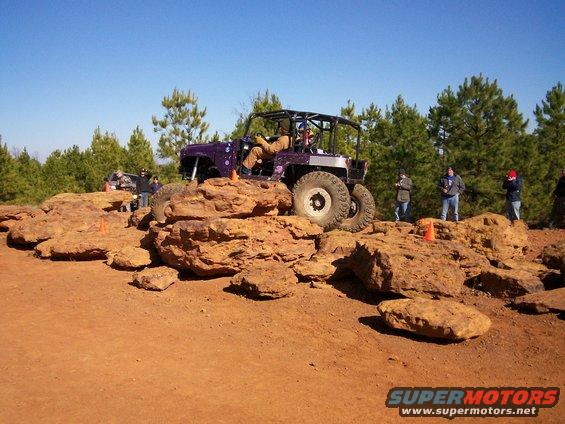 Purple off-road vehicle with a roll cage navigating large rocks