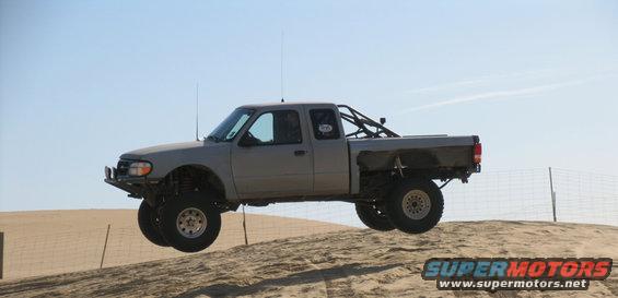 Gray Ford Ranger mid-air jump over sand dune