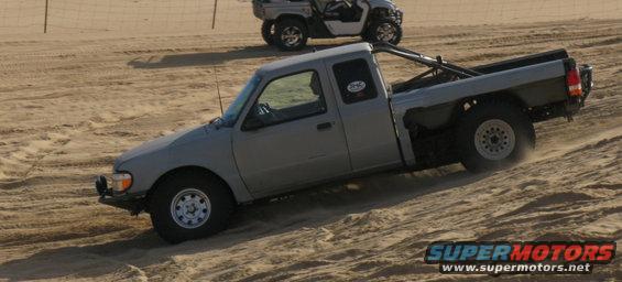 Gray pickup truck with a roll bar driving up a sand dune