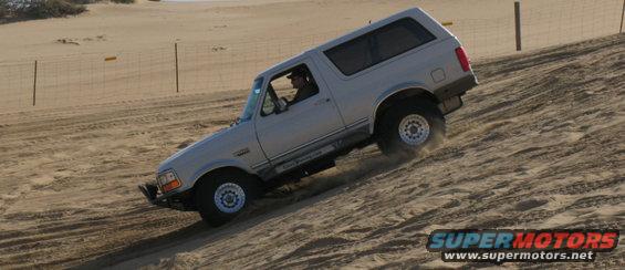Silver Ford Bronco driving up a sand dune, driver visible