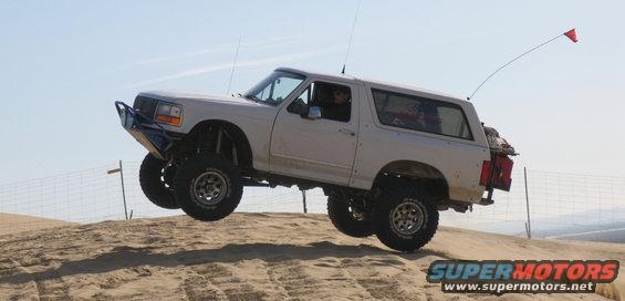 White Ford Bronco with aftermarket bumper and lift kit airborne over sand dune