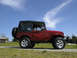 1991 Ford Bronco - This red convertible SUV is shown from a 3/4 front angle under a blue sky with wispy clouds. The Supermotors logo is visible on the lower r…
