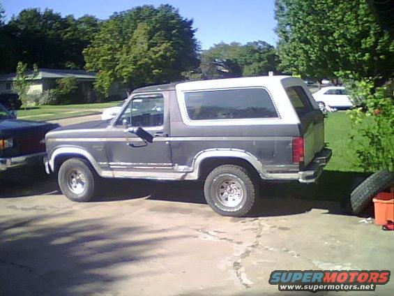 Gray Ford Bronco with white top parked on driveway. Another dark vehicle is to the left