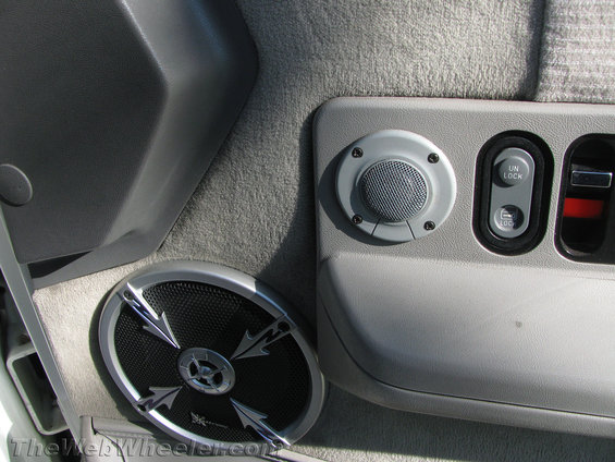 Car door panel with aftermarket speakers and power lock buttons. One speaker is round, the other is larger and oval