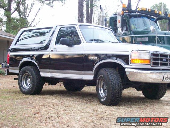 Two-tone Ford Bronco parked next to a green tow truck