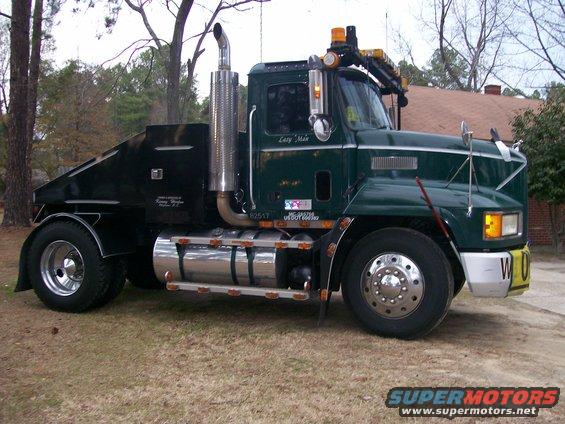 Green tow truck with a large chrome exhaust pipe and a black tow body