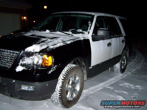 Black and white Ford Expedition covered in snow, parked on a snowy road at night