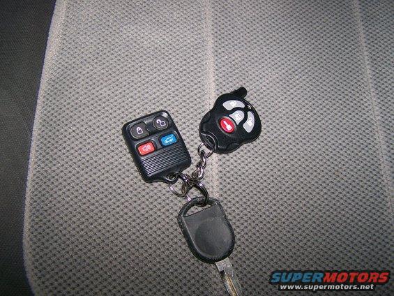 Two car fobs and a key on a keychain, resting on a textured fabric surface