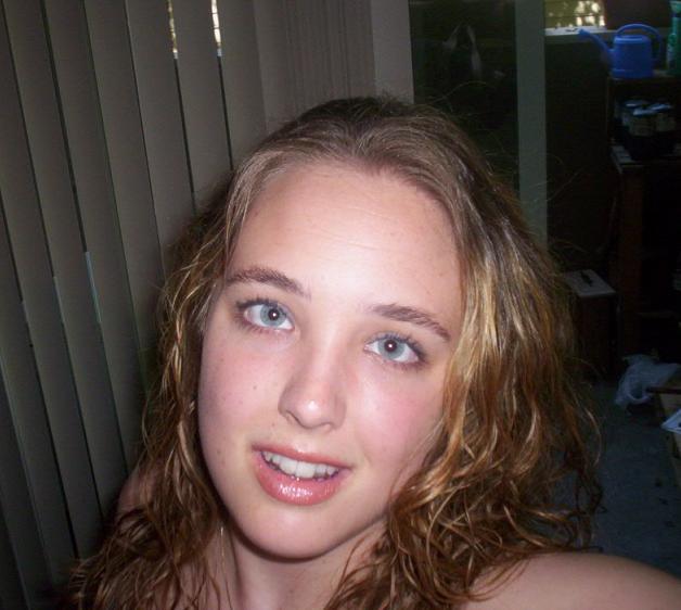 Young woman with blue eyes and curly brown hair smiles at the camera