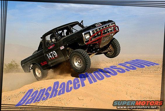 Black off-road truck with red bull bar jumping over sand dune. Number 1479 on door