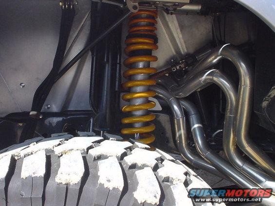 Off-road tire, yellow coilover shock, and chrome exhaust headers
