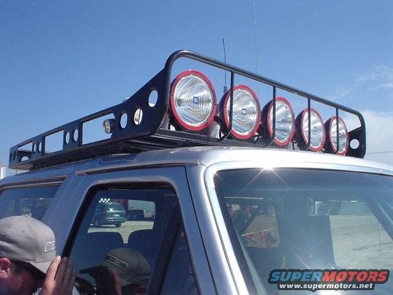 SUV with a big roof rack holding multiple large lights. Another car is visible through the side window