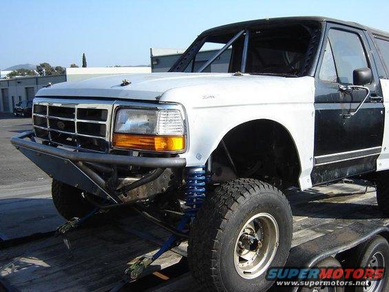 White and black Ford Bronco on a trailer, modified with a roll cage and custom bumper