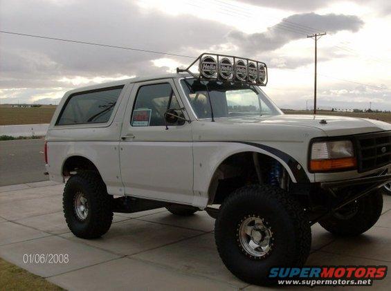 White Ford Bronco with off-road tires and roof-mounted lights, parked on a paved surface