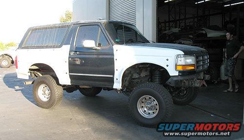 White and black Ford Bronco with aftermarket wheels, missing front bumper and fender
