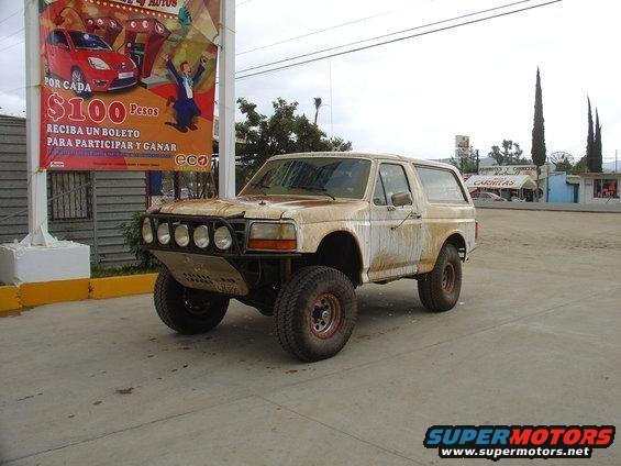 Tan Ford Bronco with off-road modifications, covered in dirt and grime, parked on pavement