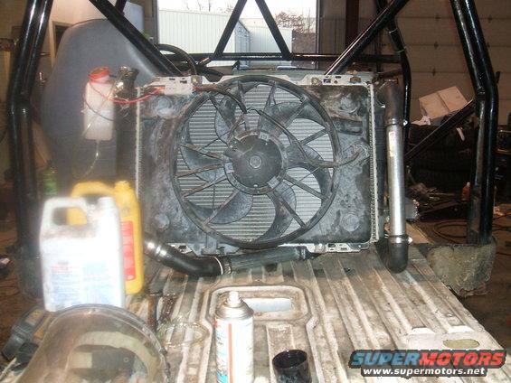Radiator and fan assembly in a vehicle's engine bay, with various fluids and a spray can nearby